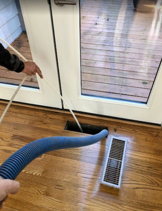 Technician cleaning air ducts through a floor vent in a residential property.