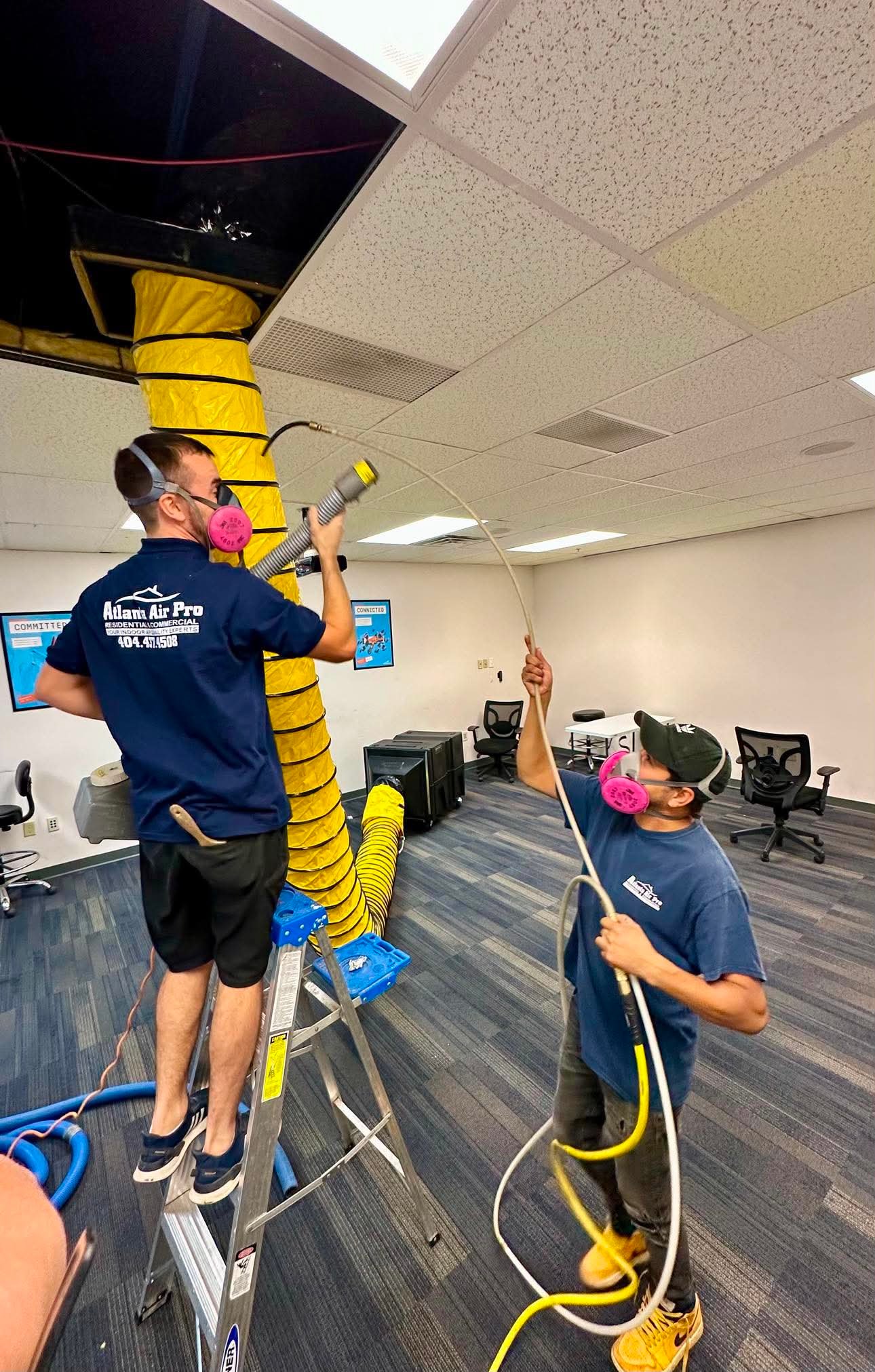 Atlanta Air Pro technicians performing commercial air duct cleaning through a suspended office ceiling using professional vacuum and agitation equipment