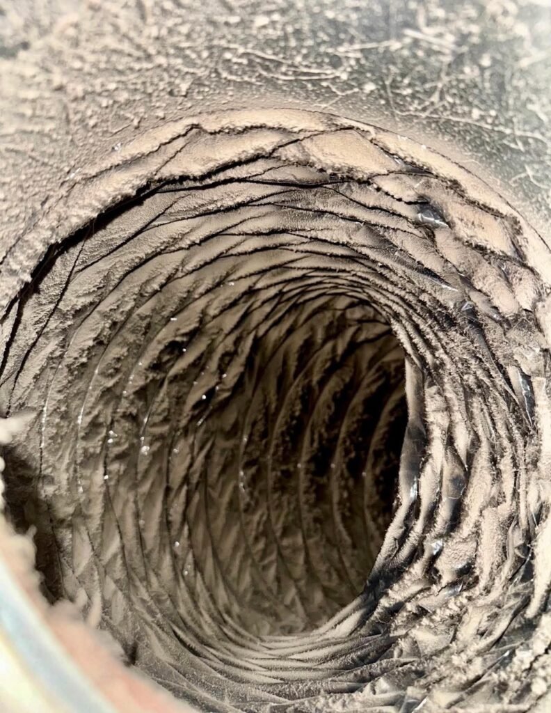 Caked dust and debris covering the interior of a curved residential flexible duct before service