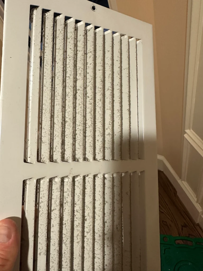 Residential air vent grille covered with accumulated dust before cleaning
