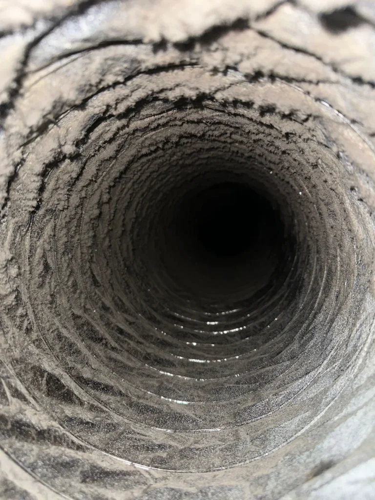 Heavy dust and debris coating the interior of a flexible residential air duct before professional cleaning