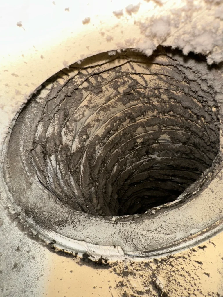 Heavy dust and debris coating the interior of a residential flexible air duct before professional cleaning